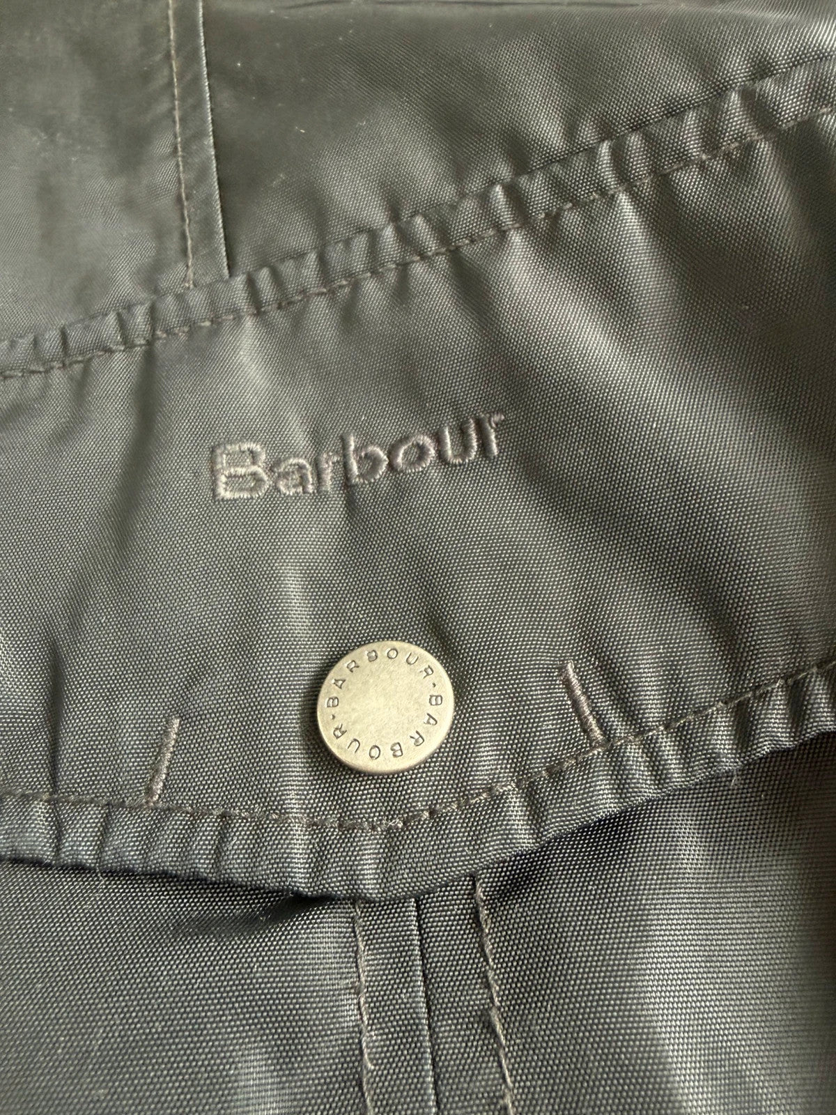 Barbour black waterproof jacket with faux fur collar, quilted shoulder panels, and tartan lining.