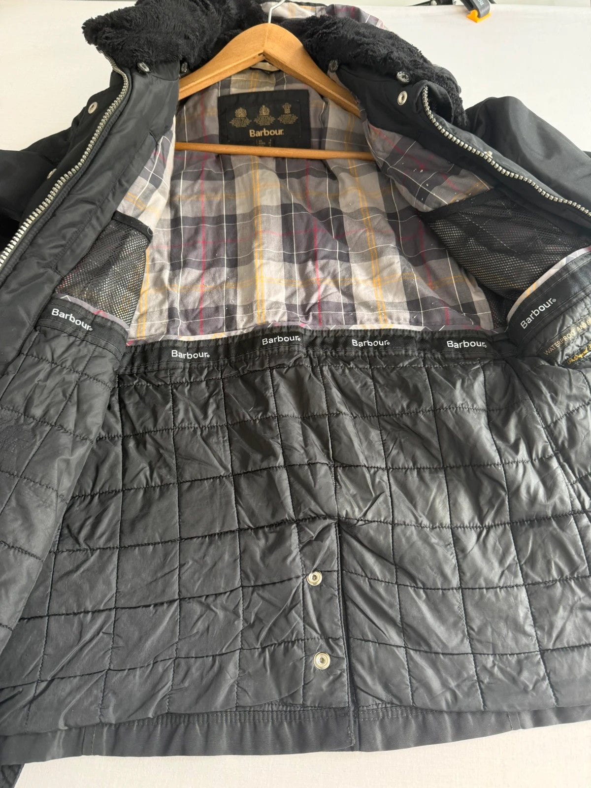 Barbour black waterproof jacket with faux fur collar, quilted shoulder panels, and tartan lining.