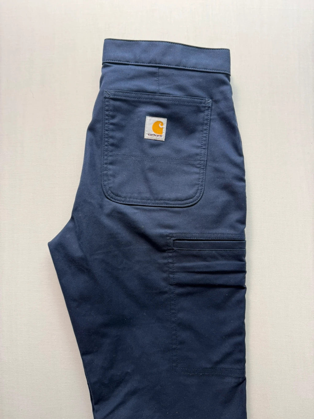 Carhartt navy work trousers with reinforced knees, multiple pockets, and Rugged Flex stretch.