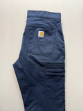 Carhartt navy work trousers with reinforced knees, multiple pockets, and Rugged Flex stretch.