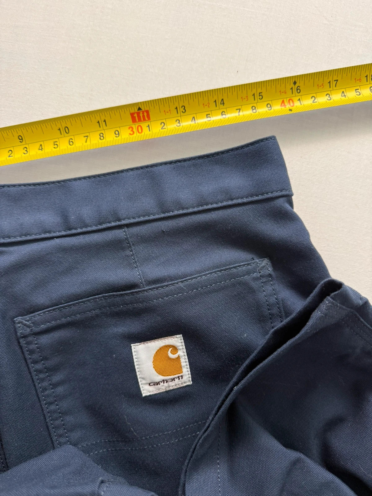 Carhartt navy work trousers with reinforced knees, multiple pockets, and Rugged Flex stretch.
