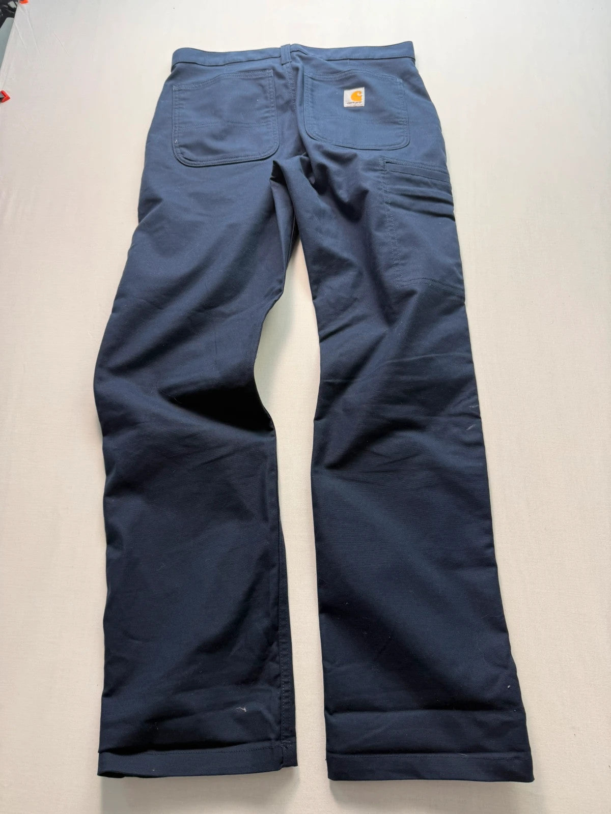 Carhartt navy work trousers with reinforced knees, multiple pockets, and Rugged Flex stretch.