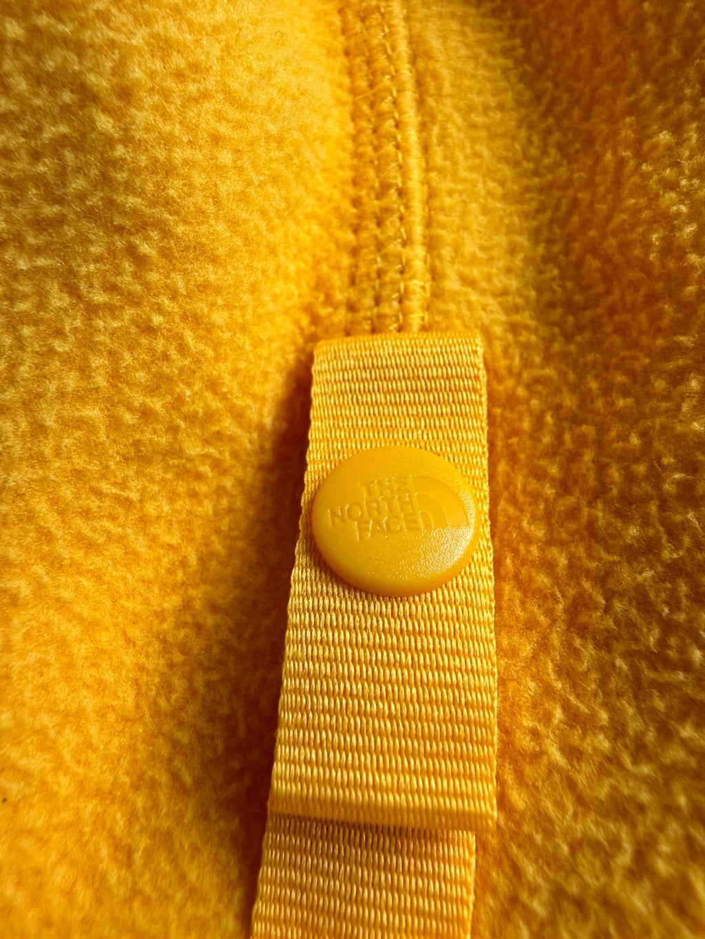 The North Face yellow fleece jacket with embroidered logo and zippered pockets.