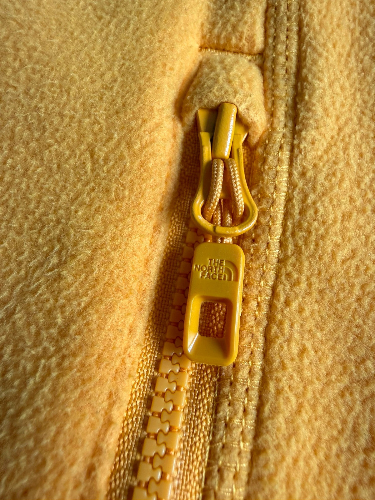 The North Face yellow fleece jacket with embroidered logo and zippered pockets.