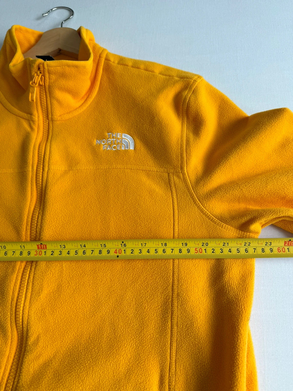 The North Face yellow fleece jacket with embroidered logo and zippered pockets.